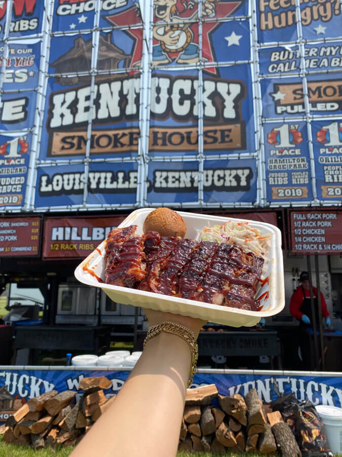 A hand holding a box of ribs with a bun and coleslaw