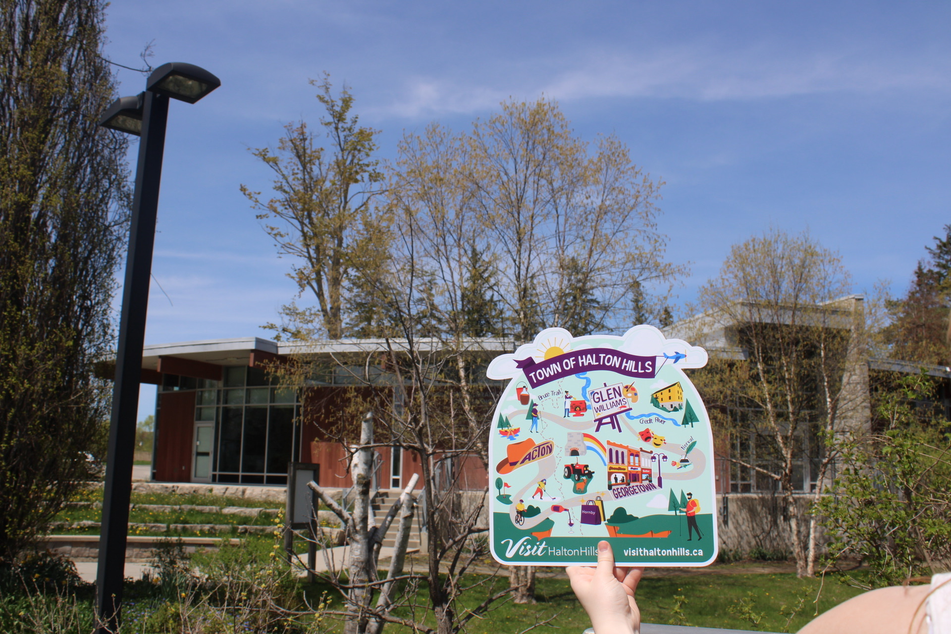 A hand holding up a large version of the sticker map. In the background is some trees and a brown building