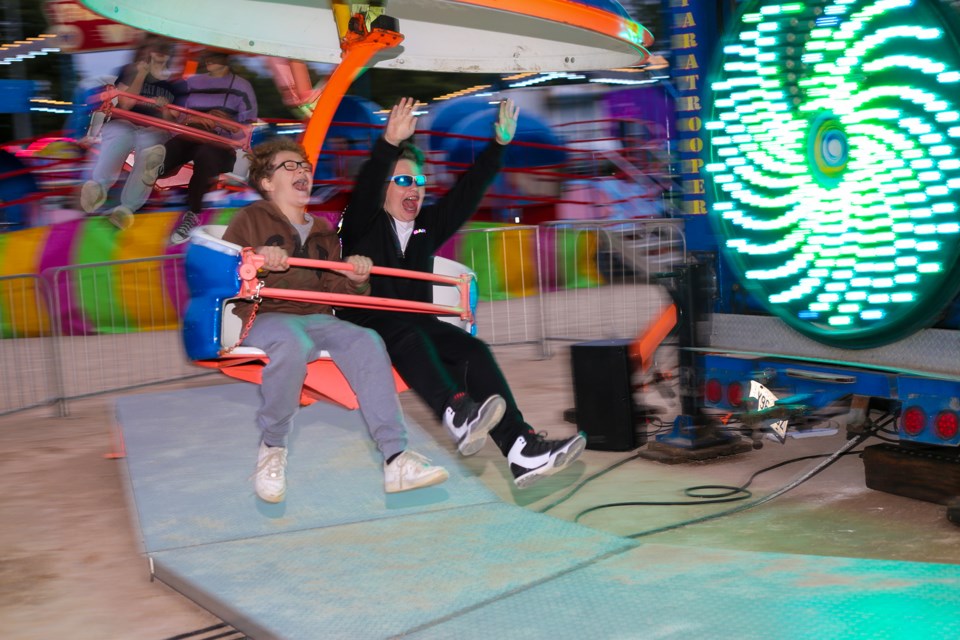 Two kids sitting in the cart of a ride that is spinning around really fast. The two kids both have excited looks on their faces. One of the children has is hands up in the air enjoying the ride