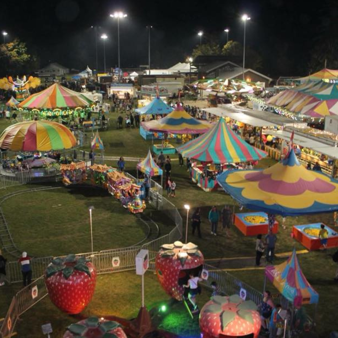 An aerial image of the Acton Fall Fair at night. You can see lots of the rides including the merry go round and spinning strawberries along with the midway games where people can win prizes