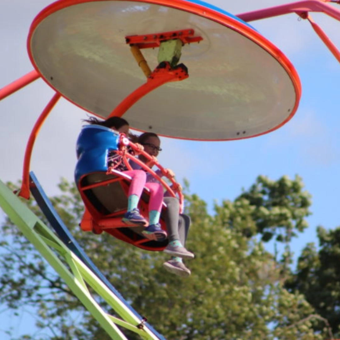 Two a mother and daughter sitting in a ride together as it spins around in the air 