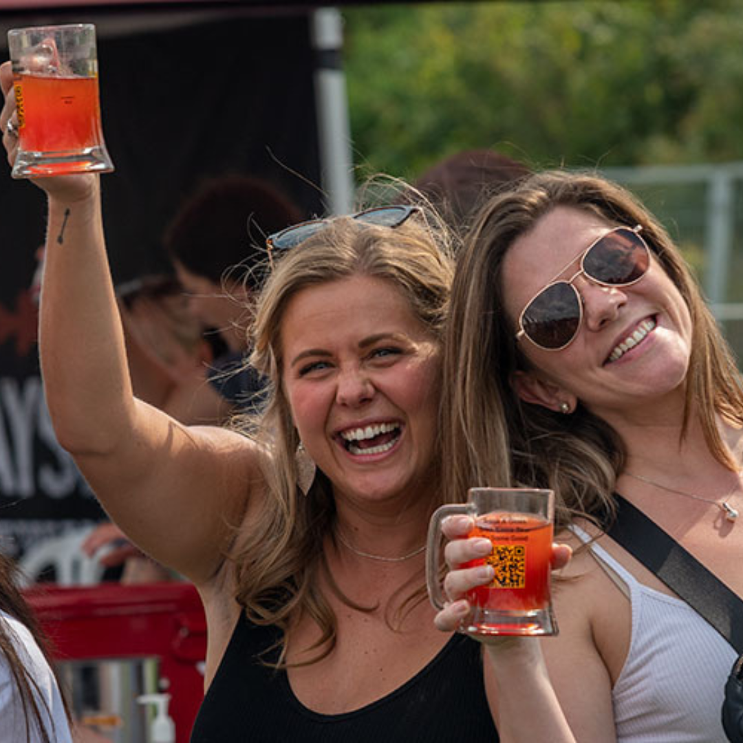 Two ladies smiling and holding steins of beer in their hands 