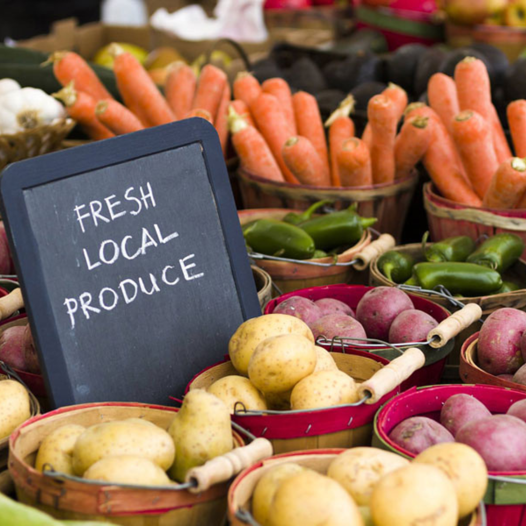 A table of fresh potatoes, peppers and carrots in buckets with a sign that says fresh local produce