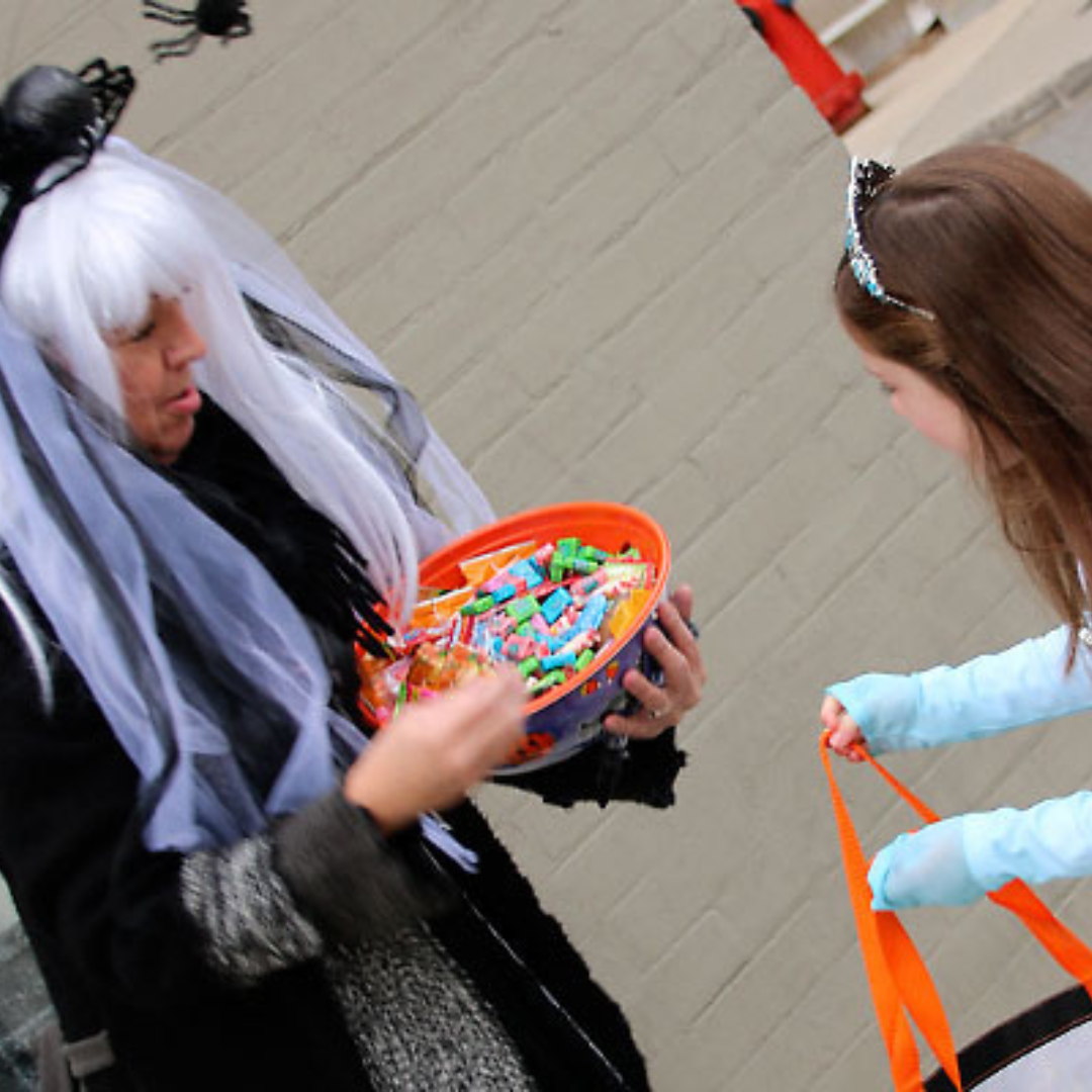 a lady in a witches costume handing out candy to a little girl